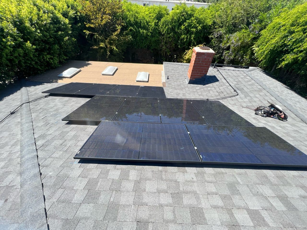 All-black solar panel installation on a composition roof with brick chimney in Los Angeles, CA